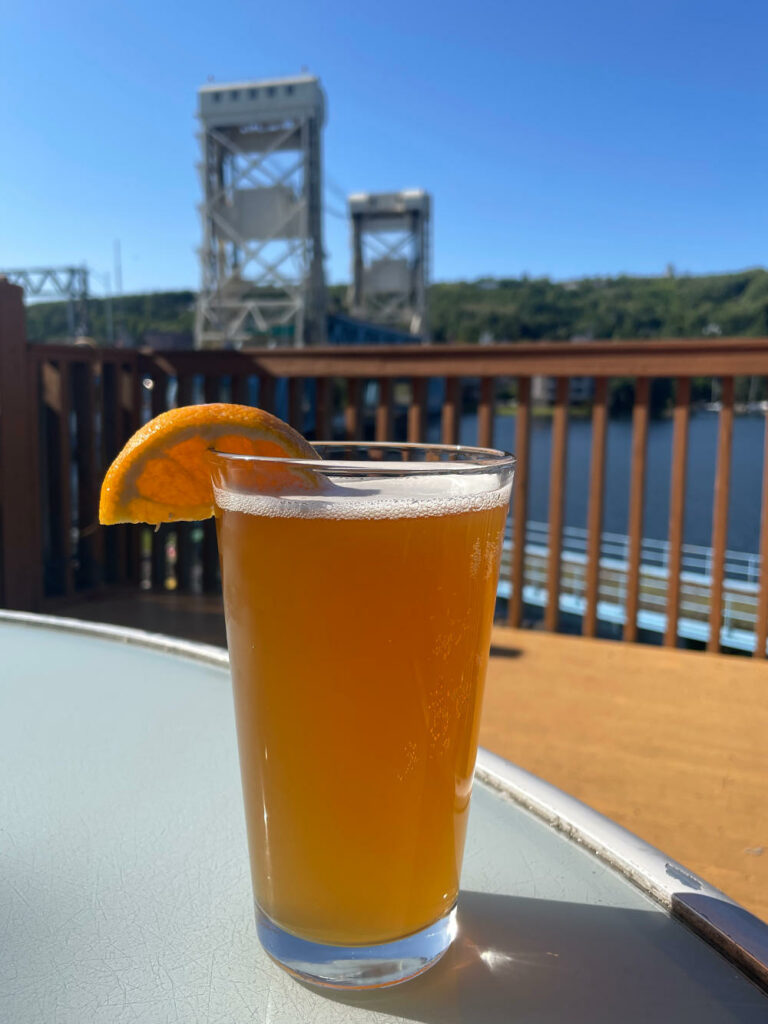 Golden beer with an orange wedge on an outdoor table in front of the Portage Lift Bridge at the Downtowner Bar in Houghton, MI