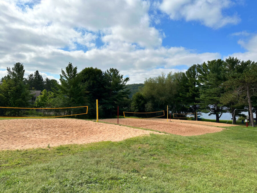 Three sand volleyball courts surrounded by pine trees at Hancock Beach in Michigan